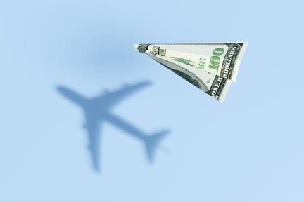 paper airplane of money with airplane shadow demonstrates the power of travel reward programs