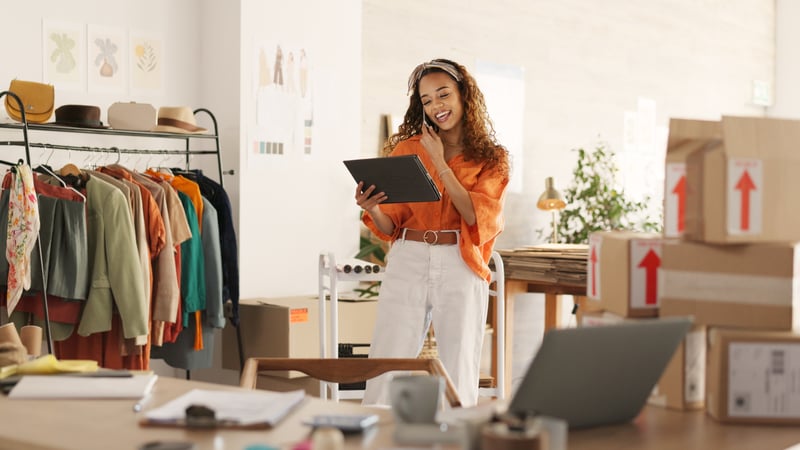 woman talking on phone while shipping items and reviewing data on tablet